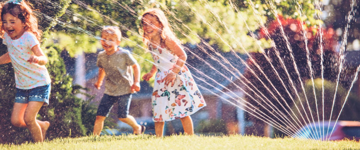 Children playing on a green lawn in Texas with a smart sprinkler system running, demonstrating healthy lawn care and efficient sprinkler system use.